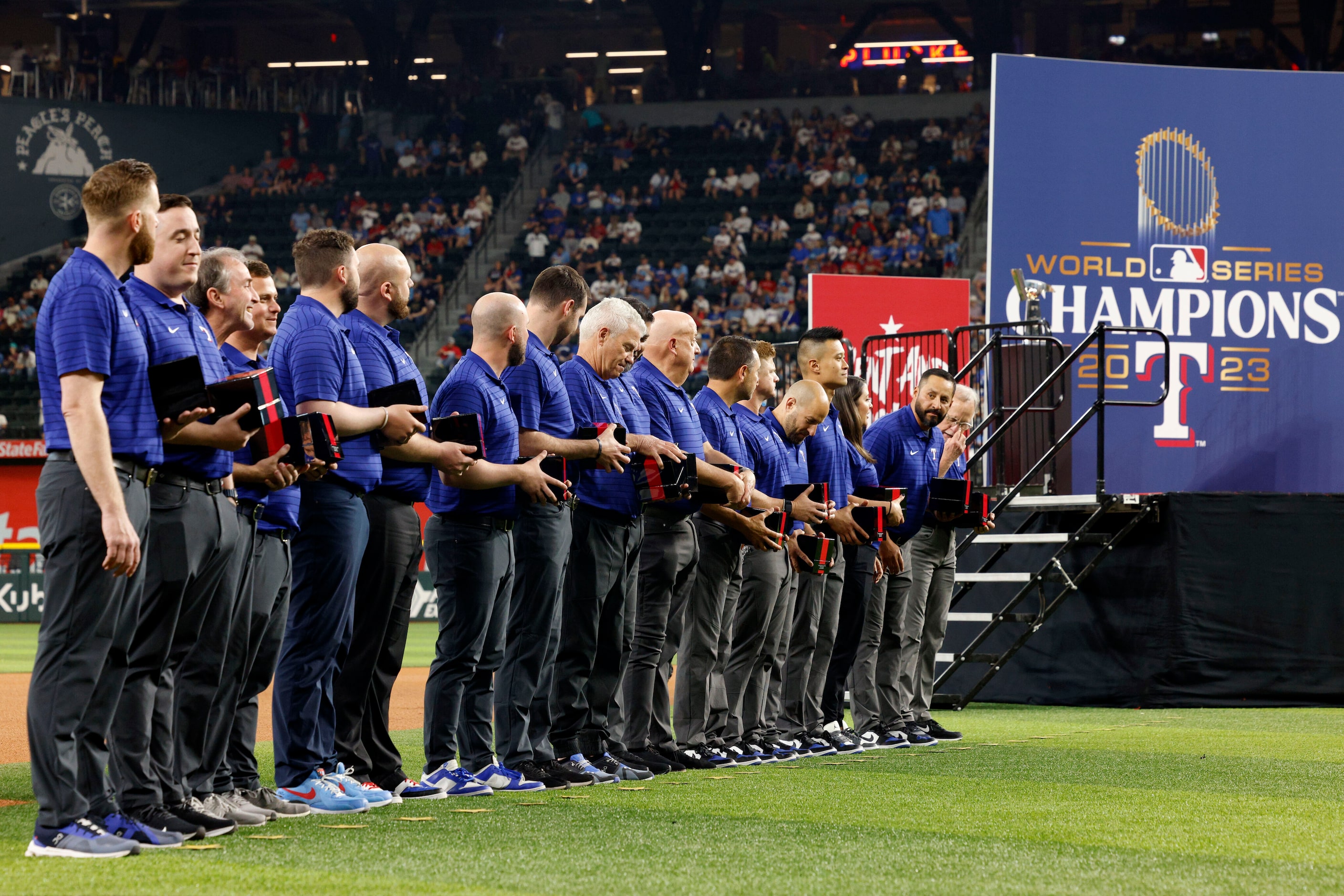 Members of the Texas Rangers coaching stand on the field with their World Series...