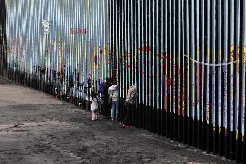A family of Central American migrants look through the US-Mexico border fence, as seen from...