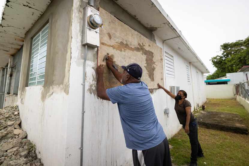 Residents attach protective plywood to a window of their home in preparation for the arrival...