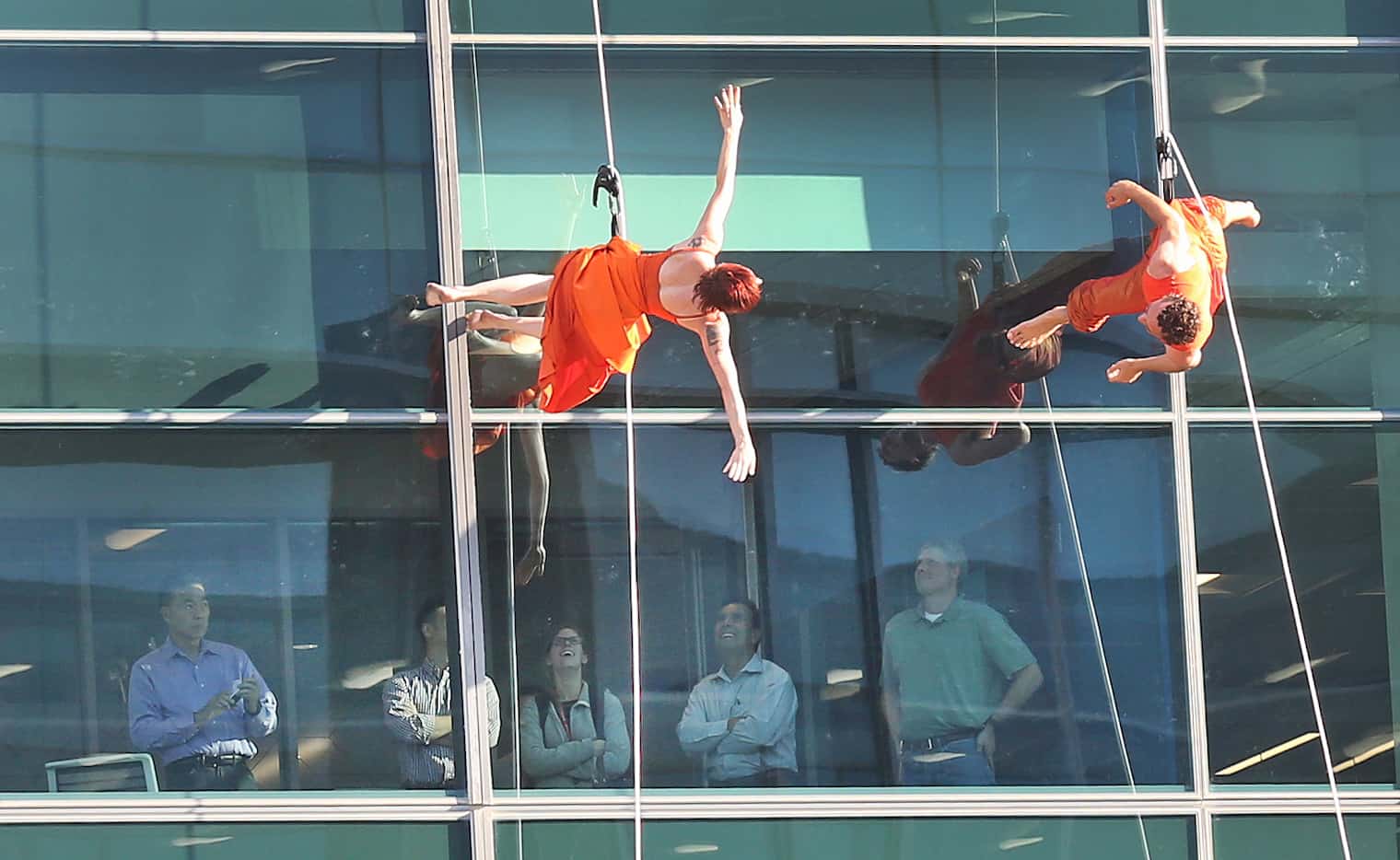 Aerial dancers perform on the Toyota building, as employees watch from their office windows,...