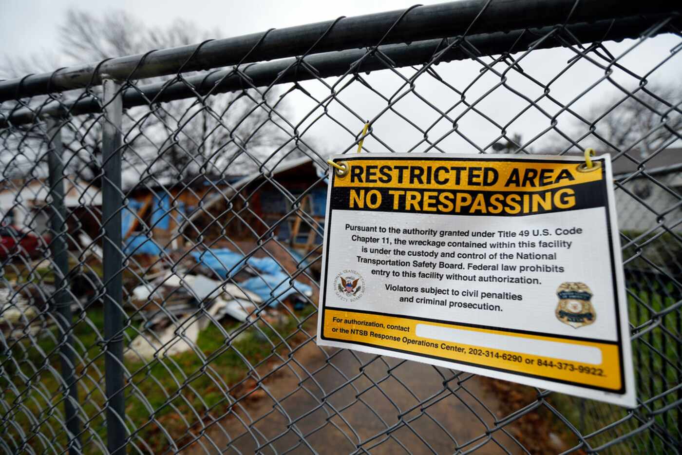 An NTSB "No Trespassing" sign hangs on a chain link fence surrounding a wrecked home in the...