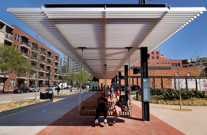 People swing on a row of wooden swings in the down West End Square park in downtown Dallas.