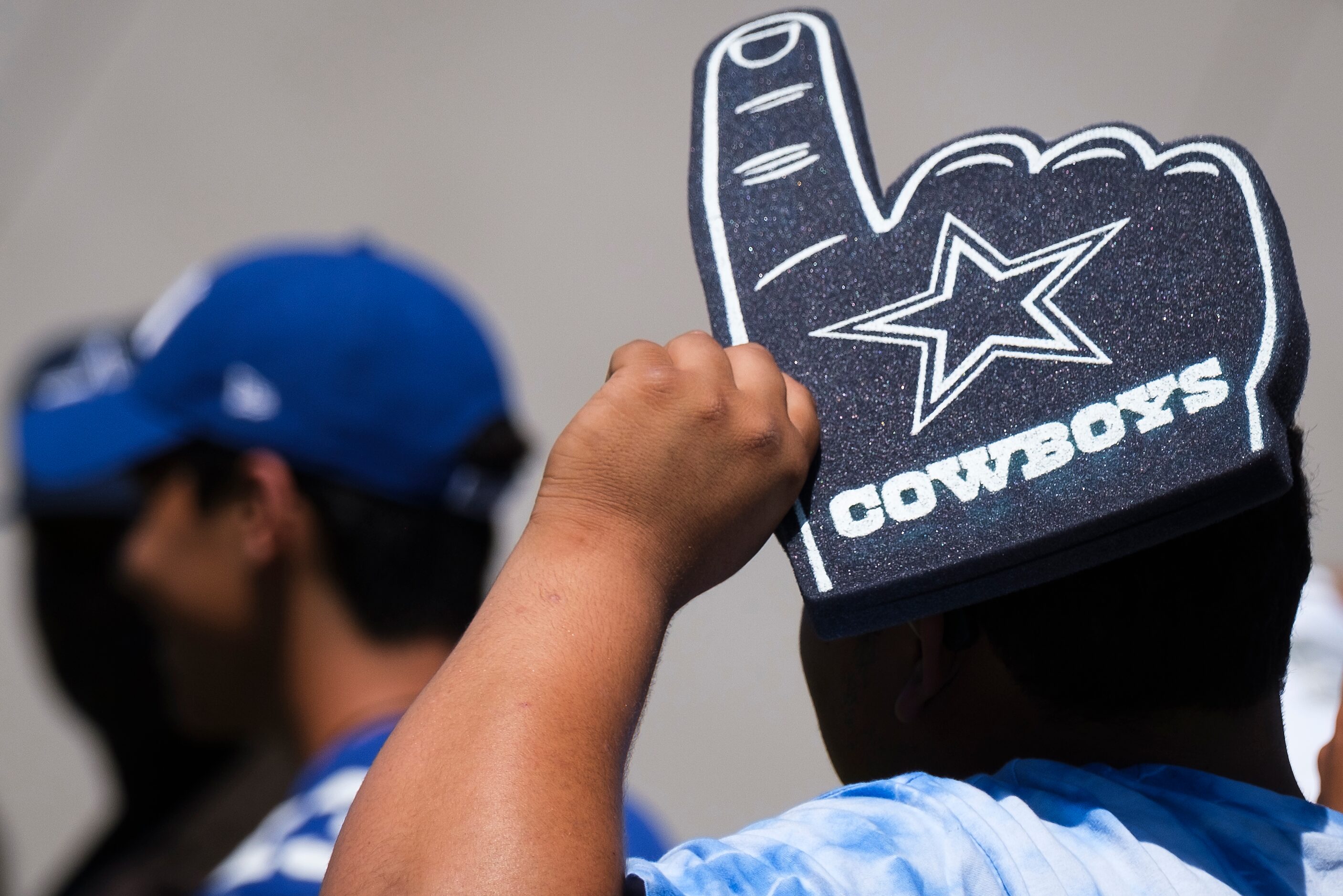 A Dallas Cowboys fan uses a foam finger to shield himself from the sun while tailgating...