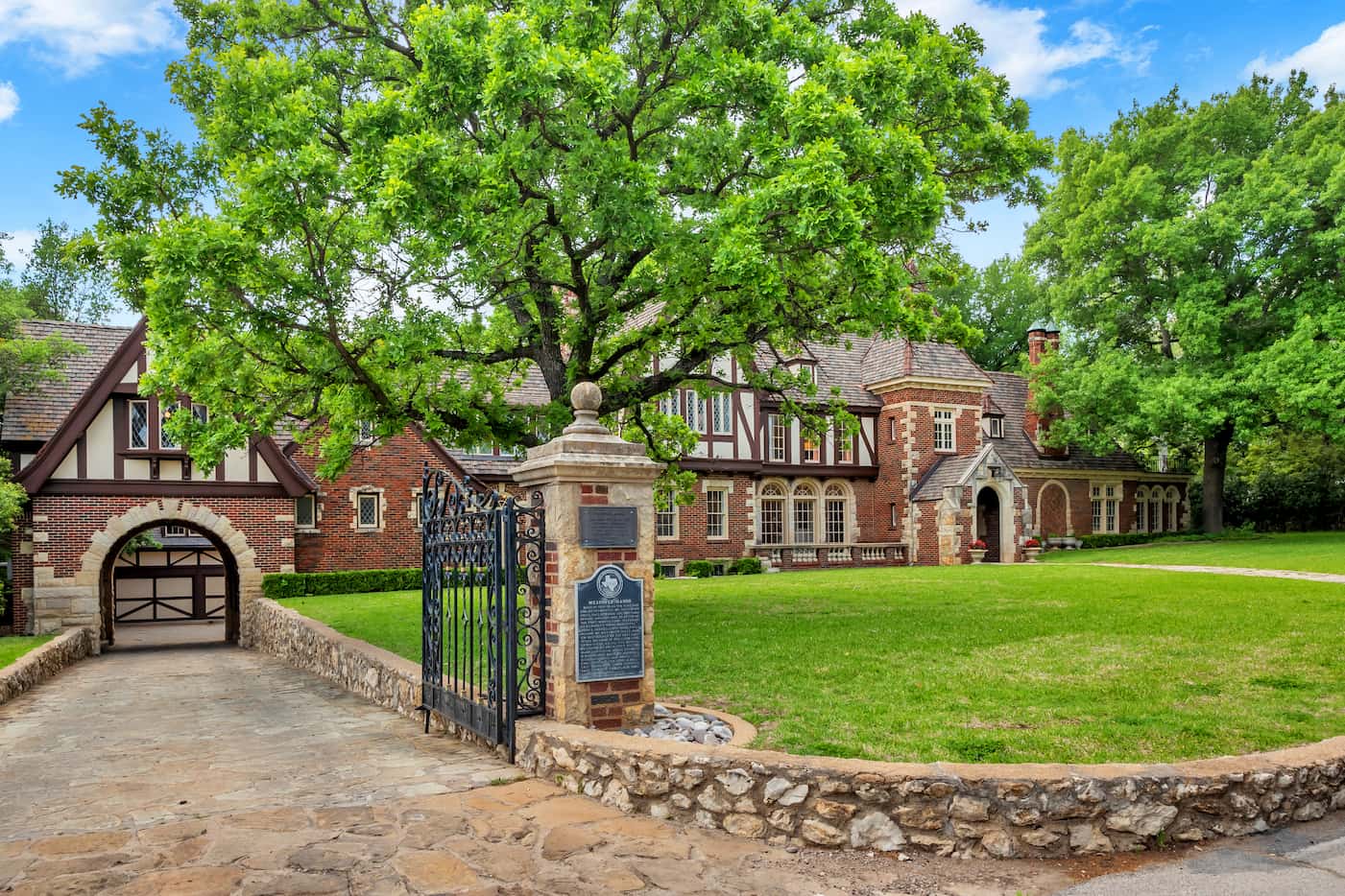 The entrance gate of a manor home is open and a plaque with historical information is...