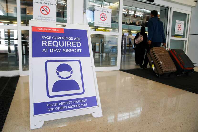 A sign notifying travelers to wear a mask as people make their way into Terminal D at DFW...