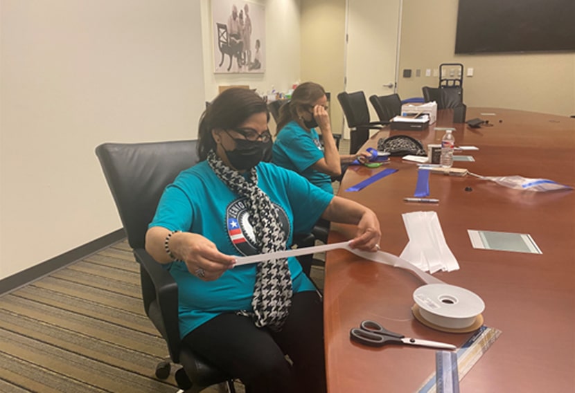 Two women volunteer with The Senior Source and sit at a table cutting fabric.