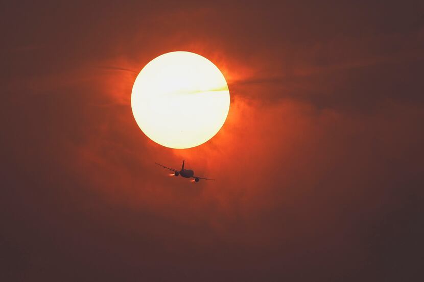 A commercial airline flies past the sun covered in haze made from smoke of Canadian...