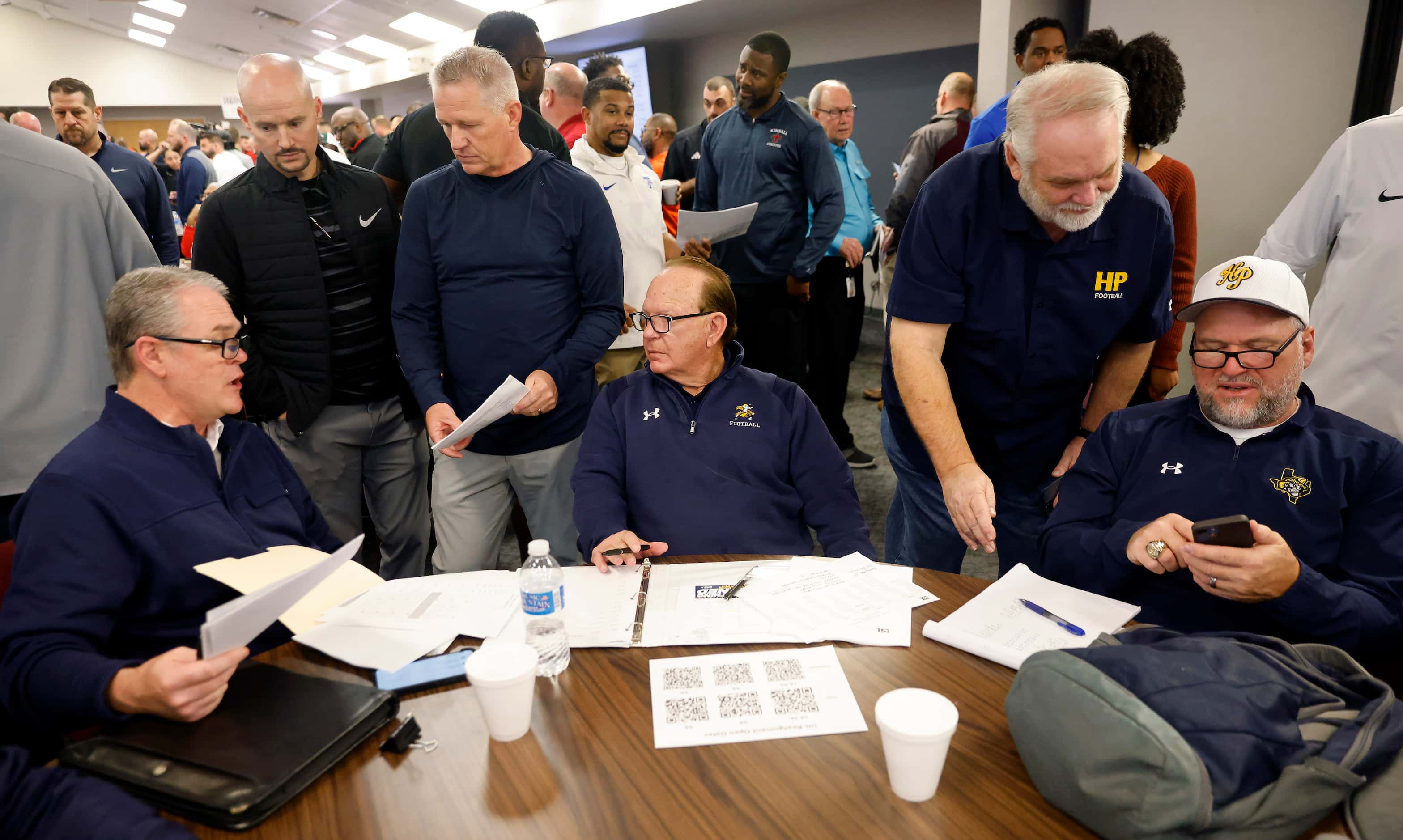 Highland Park’s staff, including head coach Randy Allen (seated, center) huddle following...