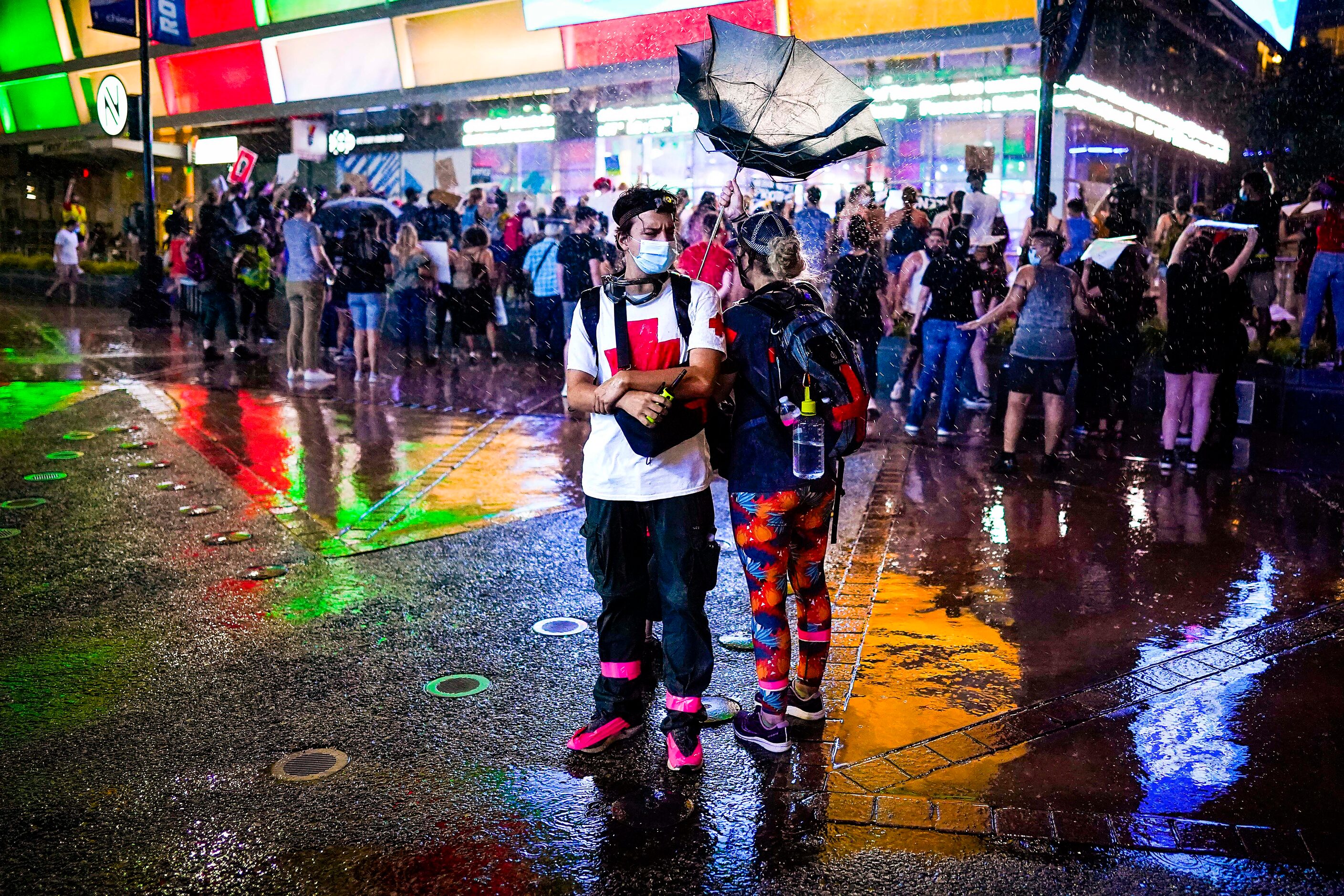 Volunteer medics huddle in the rain as their umbrella is turned inside out by the wind as a...