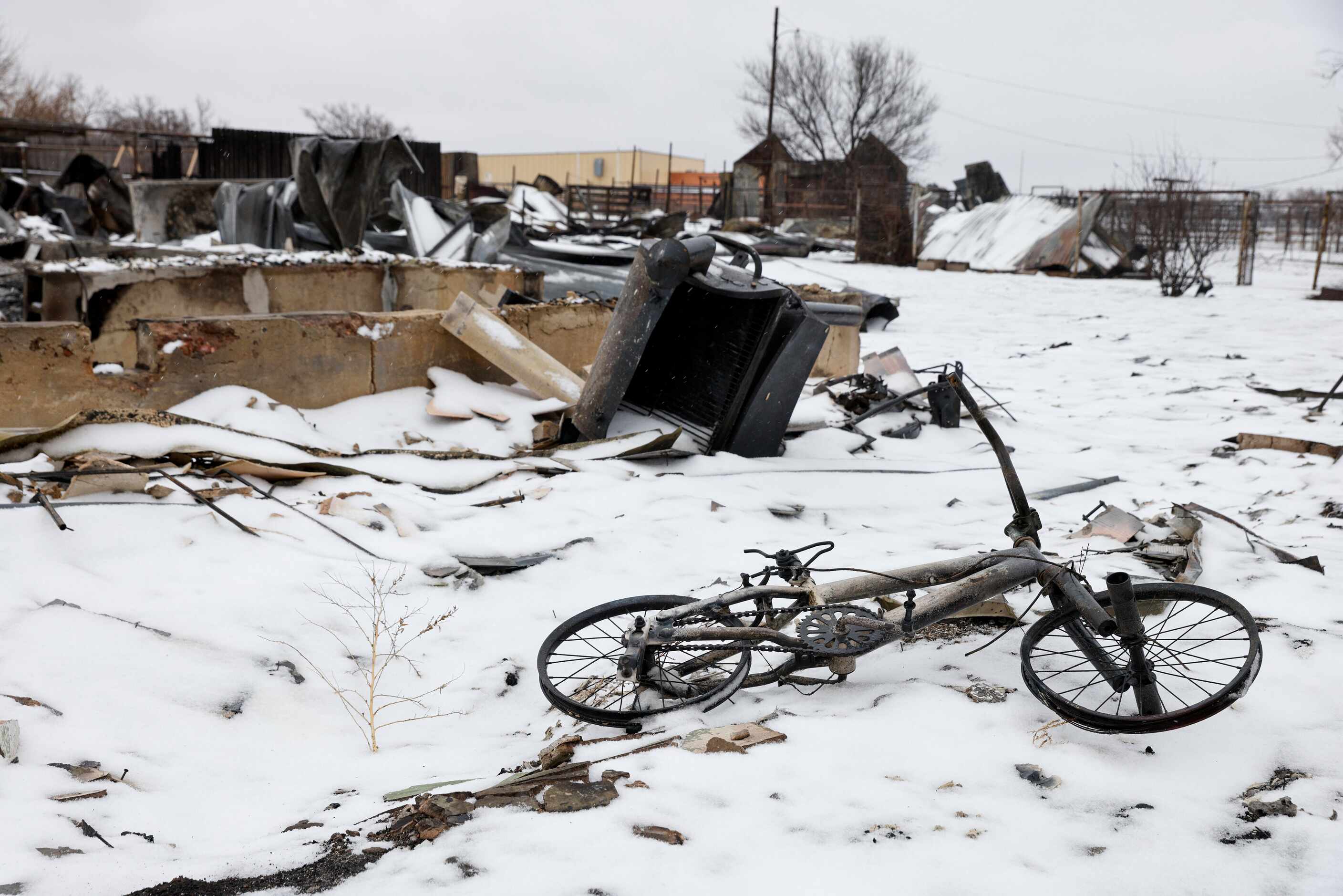 A charred children’s bicycle lays on snow-covered ground outside a home destoryed by the...
