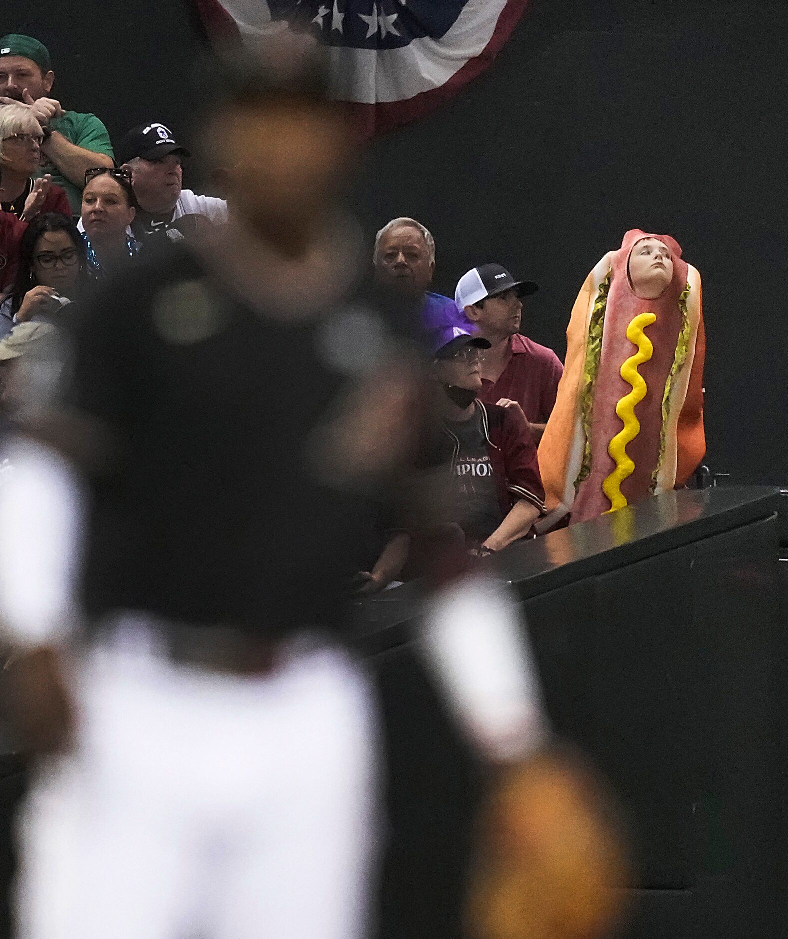 A fan dressed in a hot dog costume for Halloween looks out from the left field stands behind...