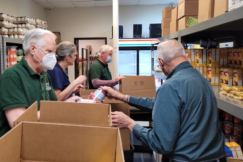 A group of older adult volunteers unpack cans out of boxes at a food pantry.