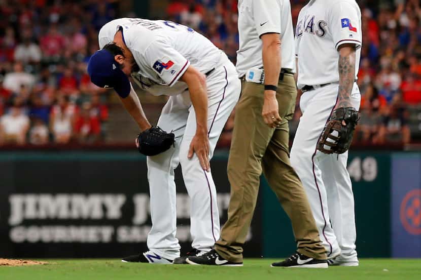 Texas Rangers' Cole Hamels touches his left leg as trainer Kevin Harmon, center, and first...