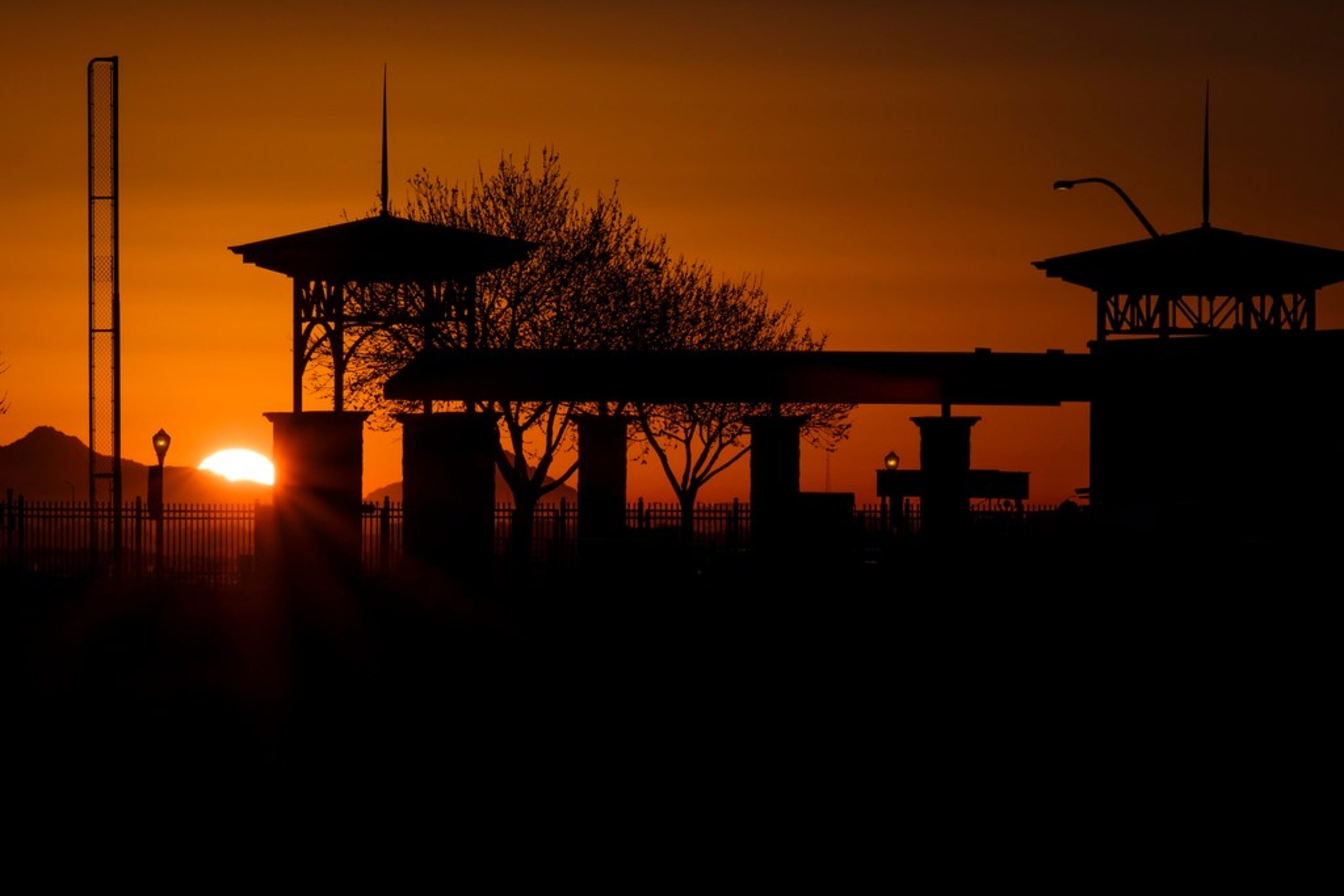 The sun rises over mountains behind the right field foul pole of Surprise Stadium on the...