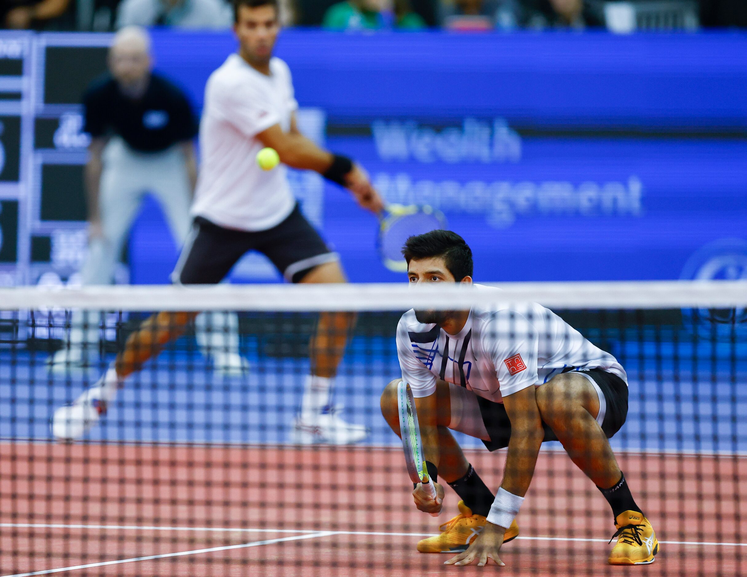 Marcelo Arevalo kneels allowing his teammate Jean-Julien Rojer to return the ball over him...