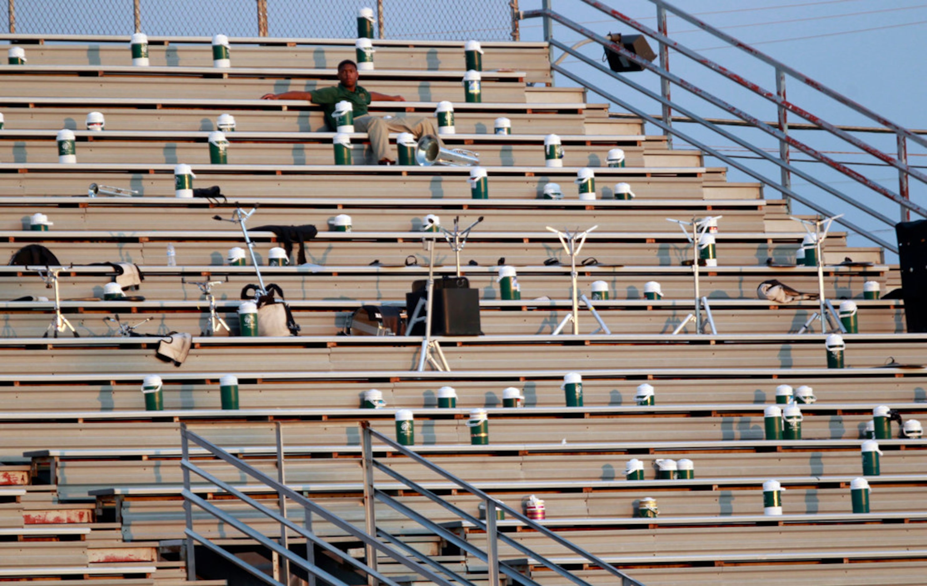 A lone Desoto band member watches over water bottles and music stands in the heat as the...