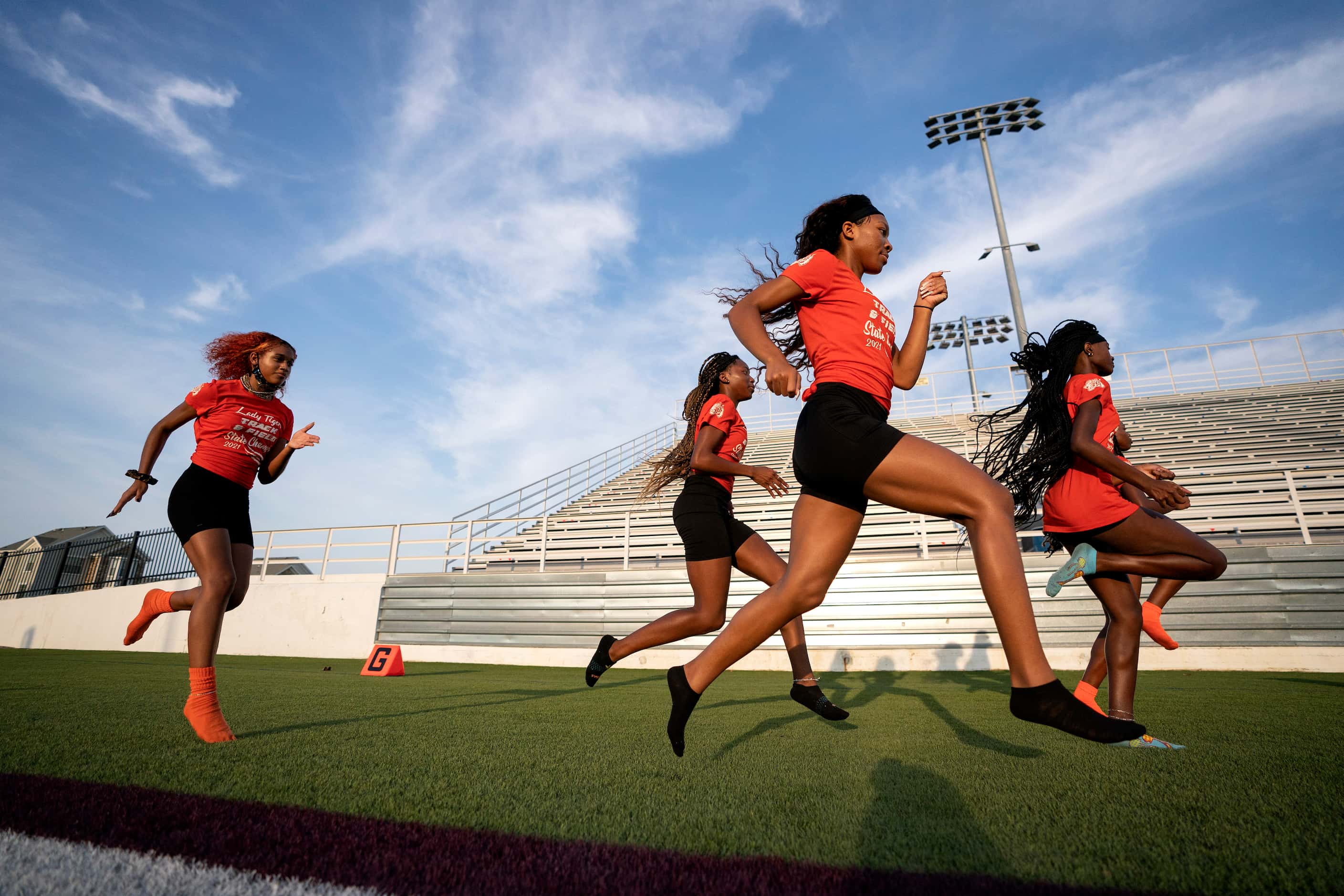 Members of the Lancaster varsity girls track team warms up to run flags before a high school...