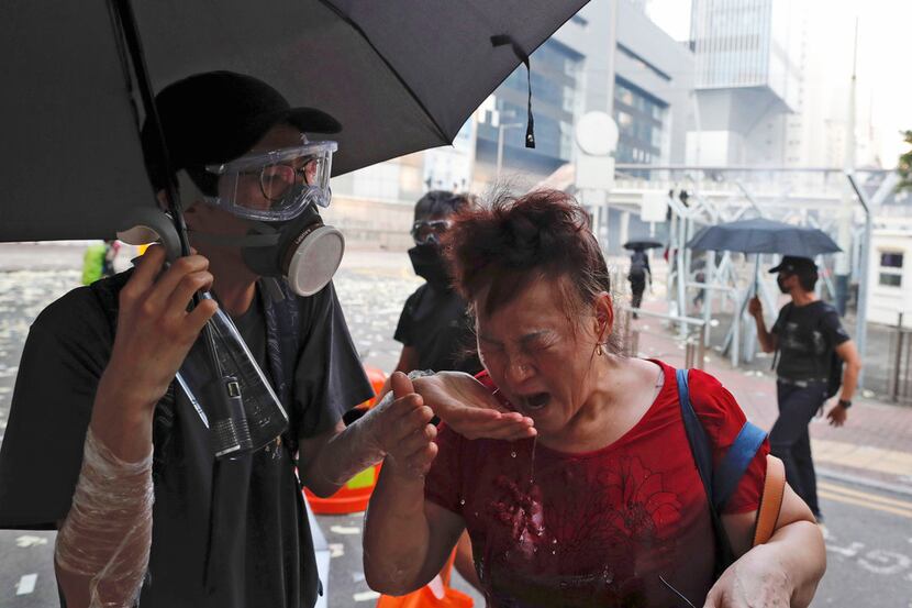 A black-clad protestor splashes water on the face of a woman after police fired tear gas...