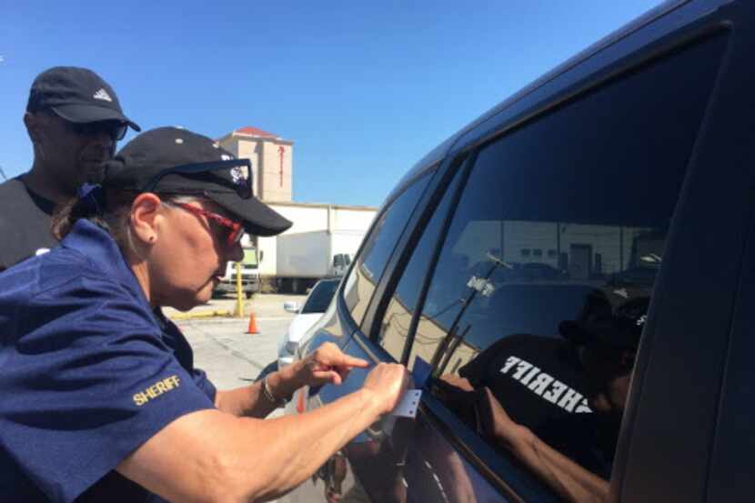 Una trabajadora de la oficina del alguacil le aplica una selladura a la ventana de un auto...