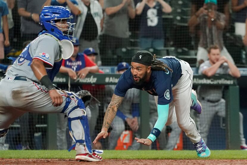 Seattle Mariners' J.P. Crawford right, dives to slide safely home past Texas Rangers catcher...
