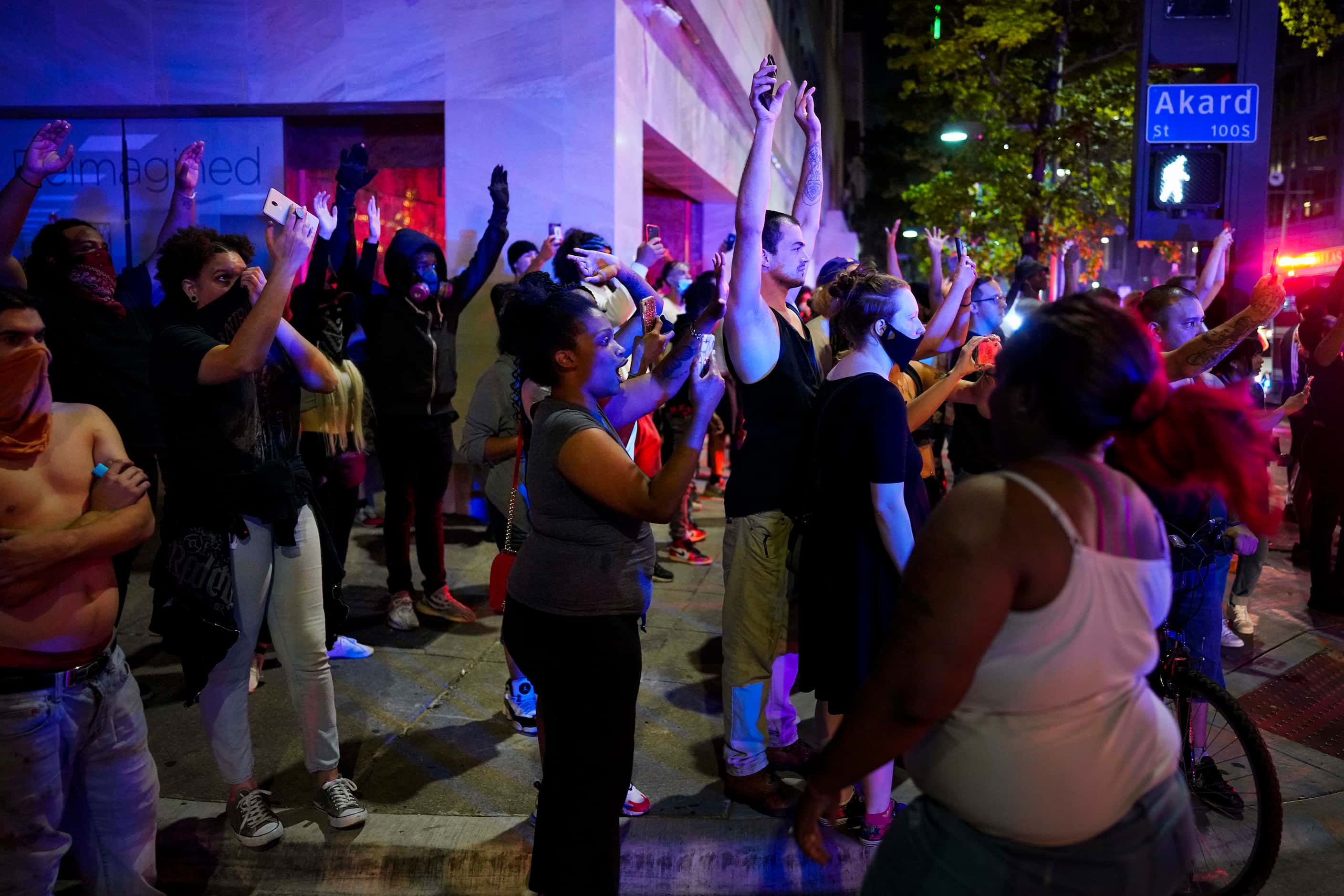 A group of people raise their hands at the corner of Akard and Main Streets downtown after...