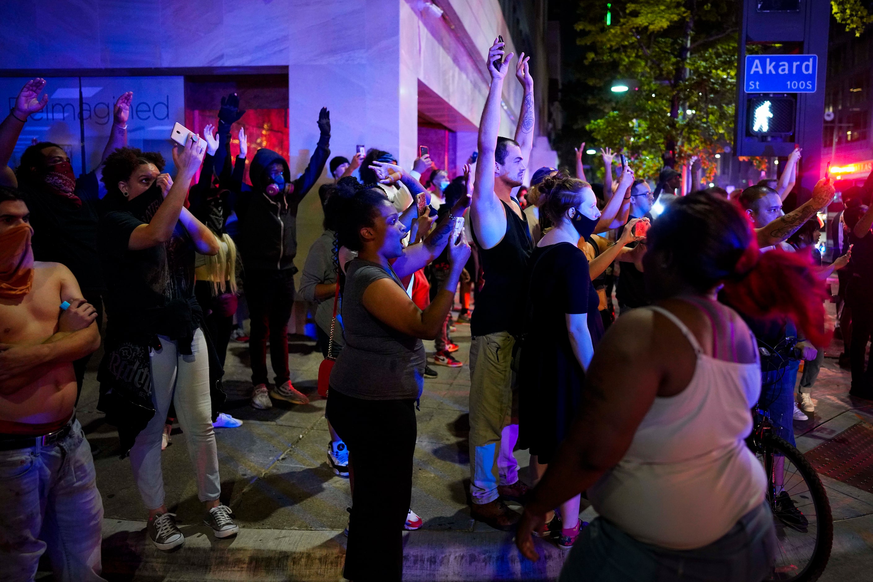 A group of people raise their hands at the corner of Akard and Main Streets downtown after...