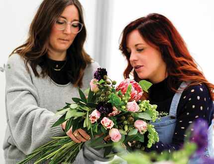 One woman hands another a floral bouquet.
