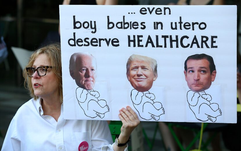 Protester Wendy Baron holds a sign featuring Sen. John Cornyn (R-TX), President Donald Trump...