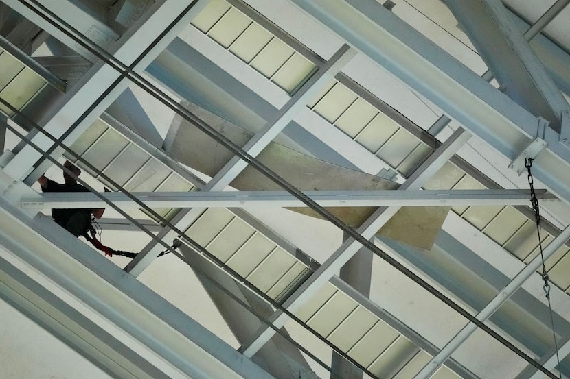 A stadium worker works to secure a loose piece of metal to the catwalk of AT&T Stadium after...