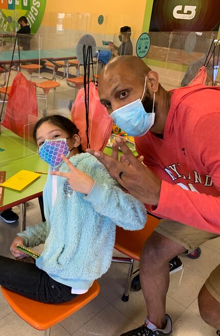 A Dallas Afterschool student and instructor wearing masks hold up two fingers each in peace...