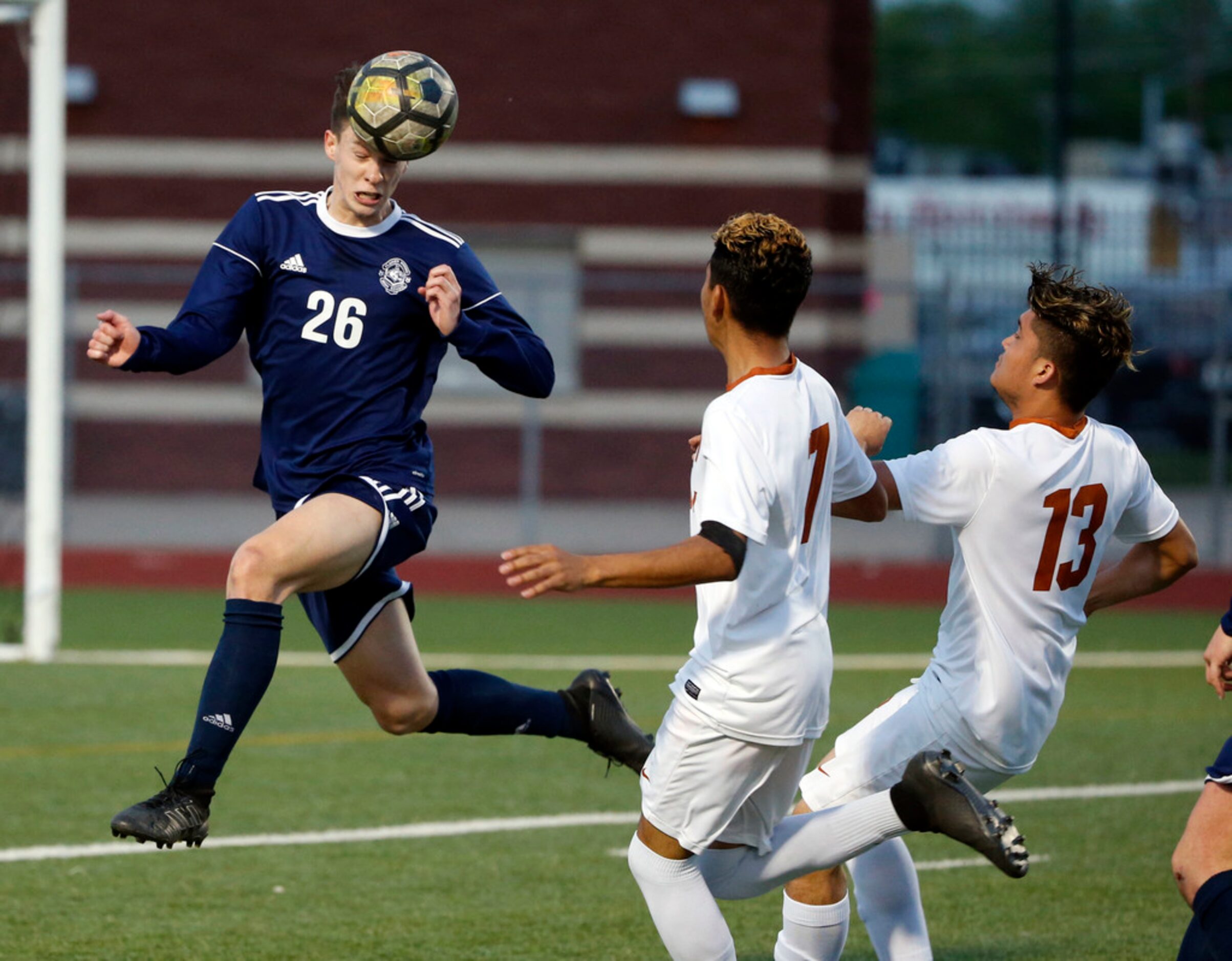 Flower Mound's Wyatt Brennan (26) heads the ball away from W.T. Whit's Angel Escorza (7) and...