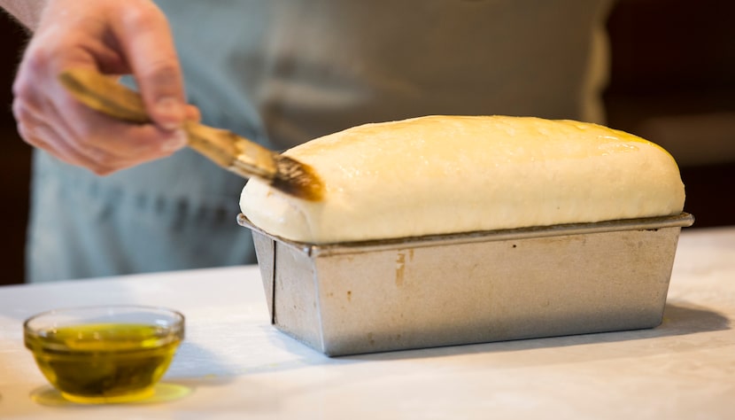 Chef Joe Baker coats the top of a bread loaf in oil as he and his son, Blais Baker, 5, host...