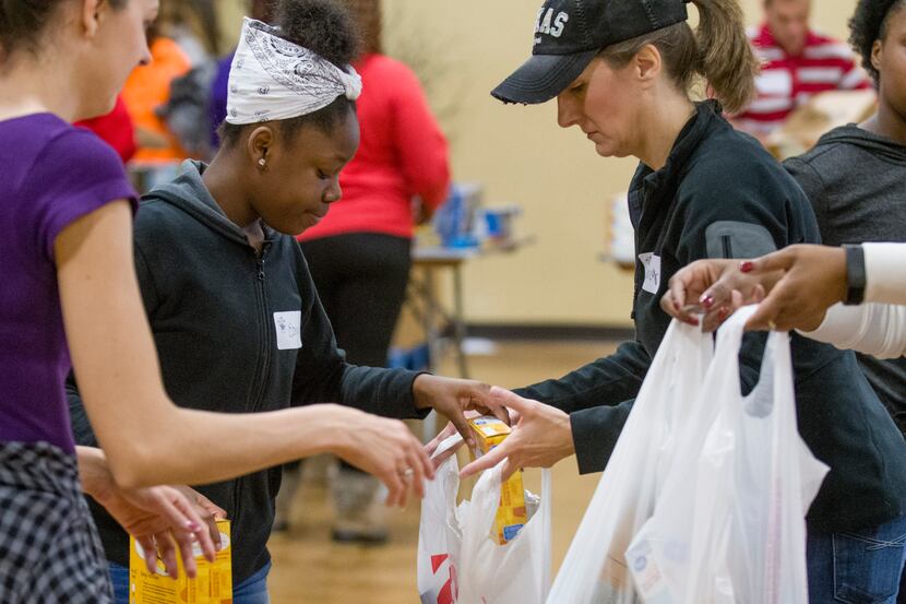 Volunteers at Youth World fill bags of groceries for 300 needy families who received food...