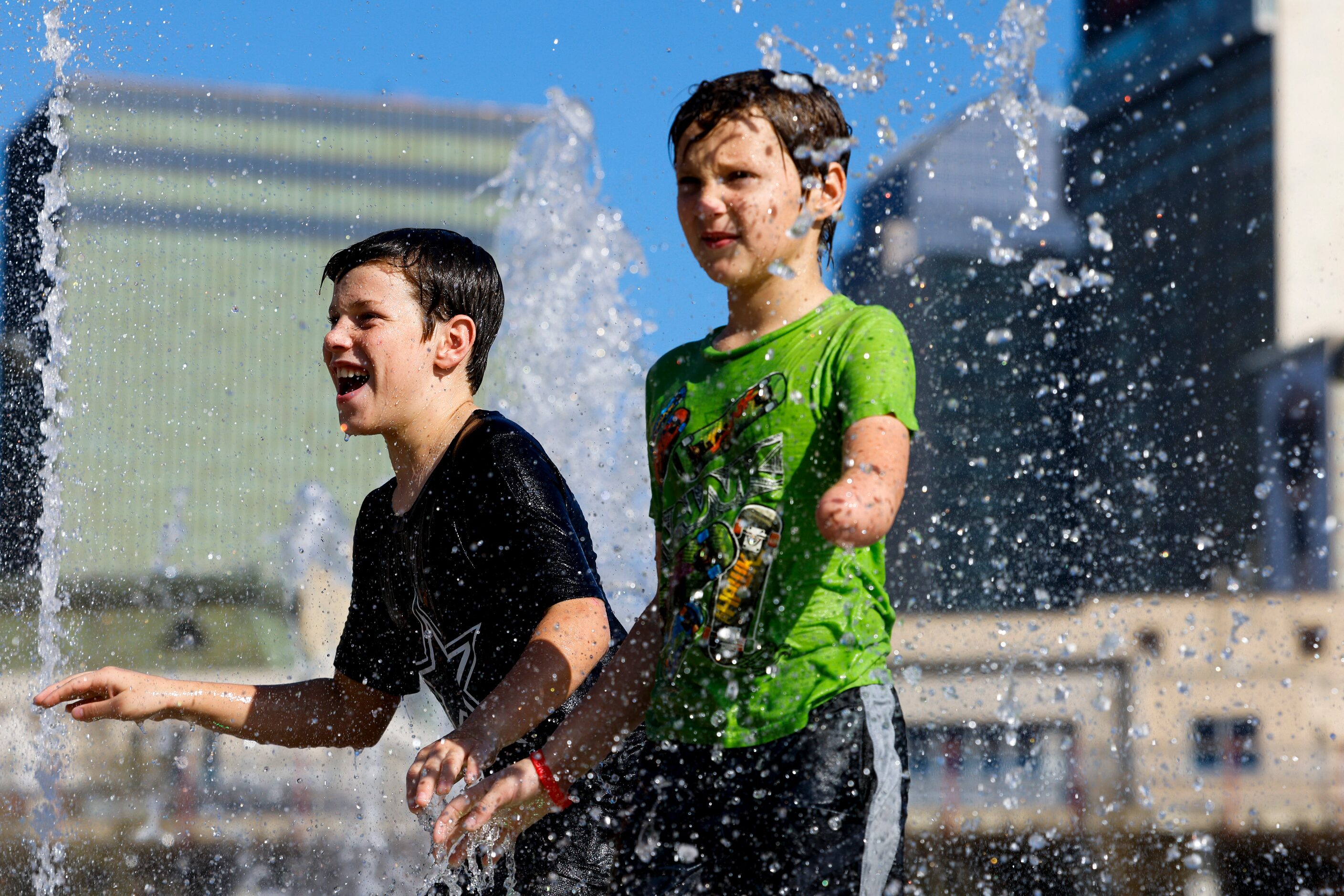 Creed Trulson, 13, (left) and his brother Sage play in the water fountain during the opening...