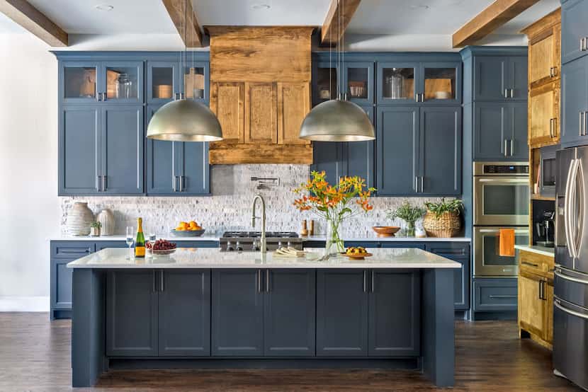 Luxury kitchen with blue-gray cabinets and island and stained vent hood, with nickel light...