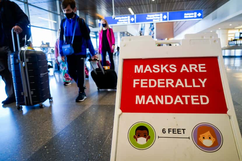 Travelers pass signs advising of the federal mask mandate on planes and at airports due to...