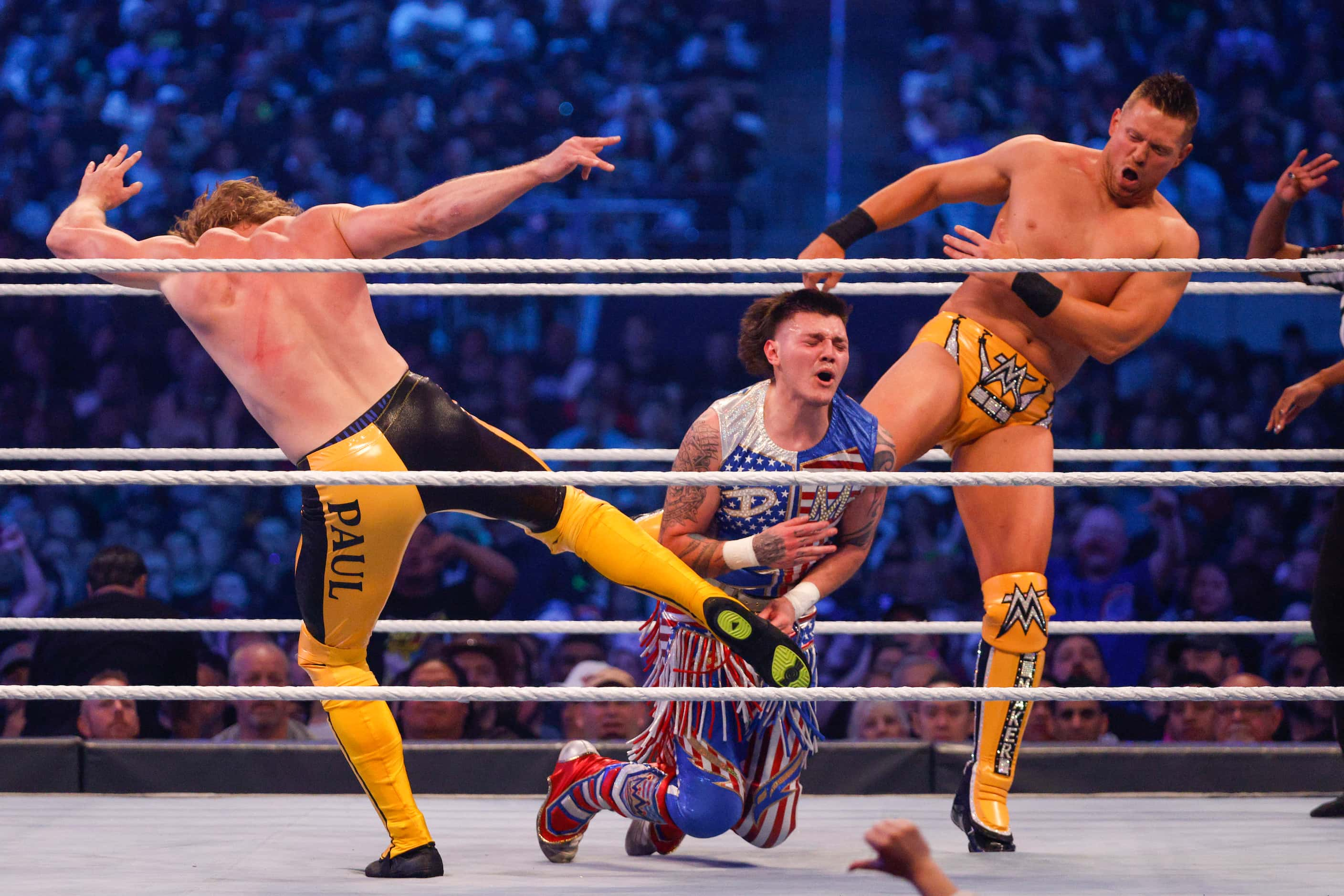 Logan Paul (left) and The Miz (right) kick Dominik Mysterio during a match at WrestleMania...