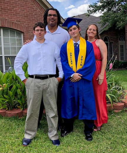 A young man in a graduation gown poses with his mother, father and brother on the lawn in...