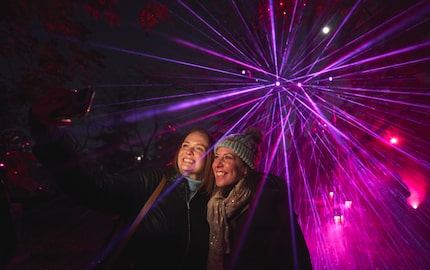 Two women dressed in warm clothes take a selfie together amidst purple laser lights all...