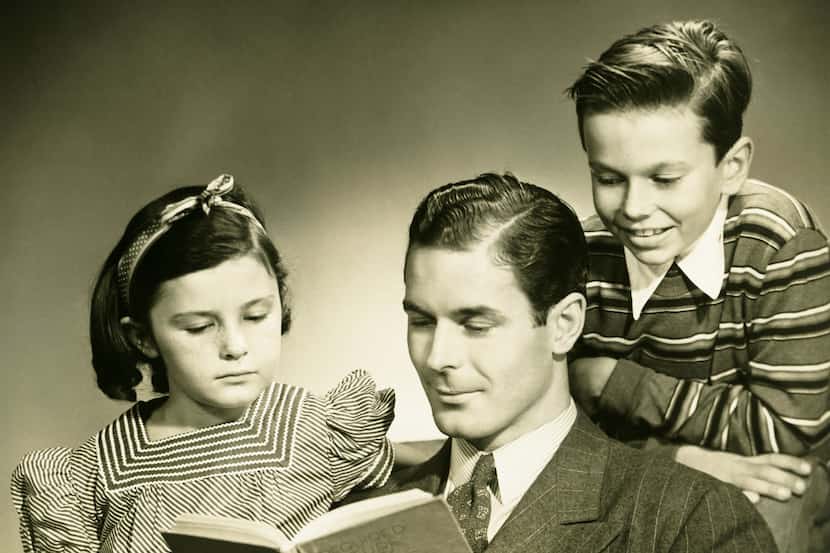 Father reading to son (4-5) and daughter (6-7) in studio, (B&W), portrait