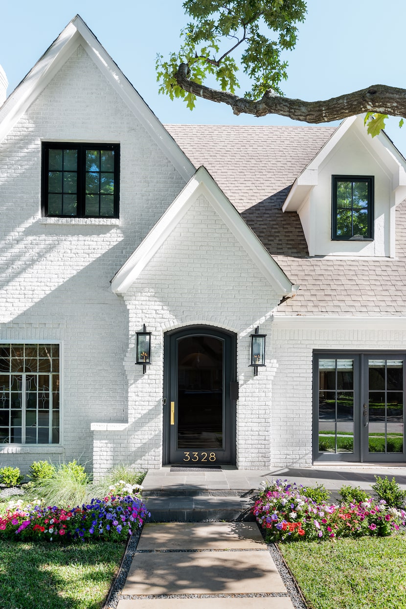 A home's brick is painted white and there are fresh flowers in the front yard.