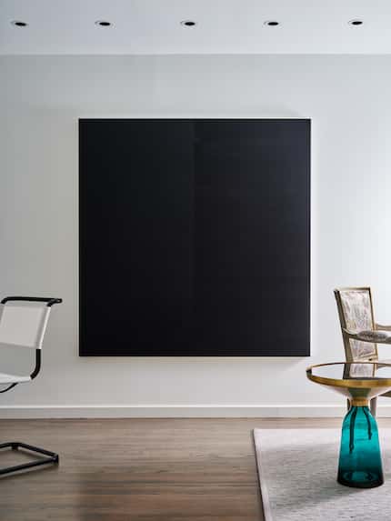 A black piece of artwork hangs on a white wall.