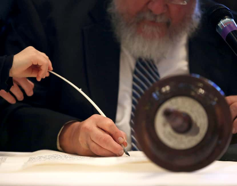 A child holds the end of the scribe's quill as he writes as a way to participate in the...