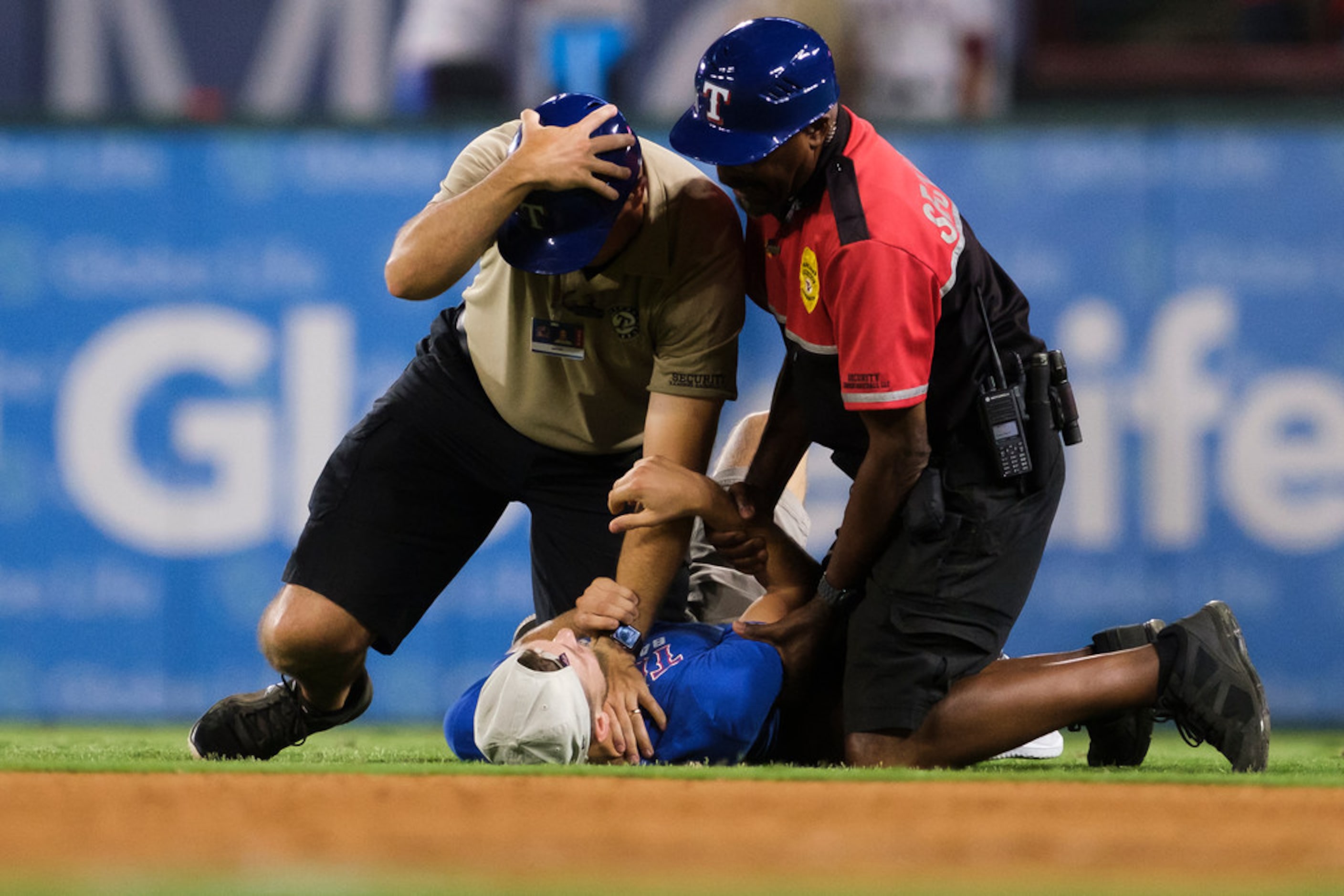 A security guard holds down a fan who ran on to the field during the ninth inning of a game...