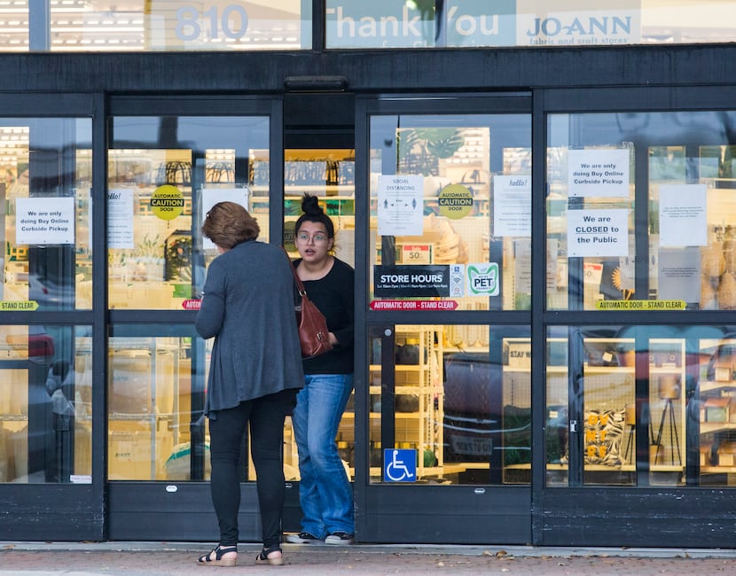 An employee talks to a customer at the front door entrance where signs are posted at Joann...