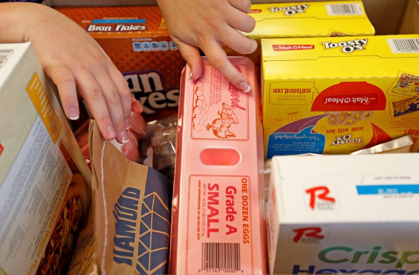 A volunteer puts groceries into a box for clients at Crossroads Community Services.