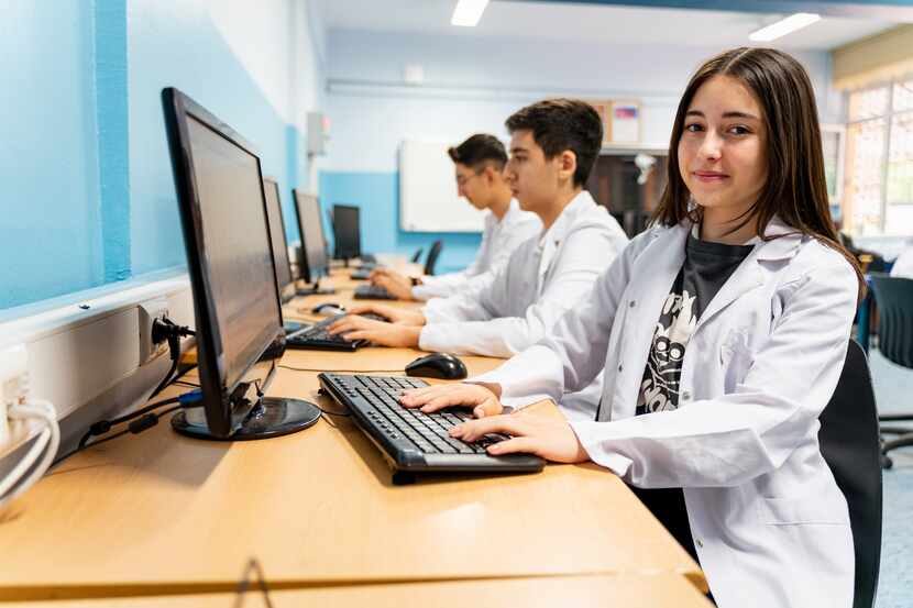 Students in white lab coats work on computers.