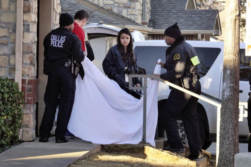 
Dallas Police Department officers use a sheet to cover the doorway as the body of a...