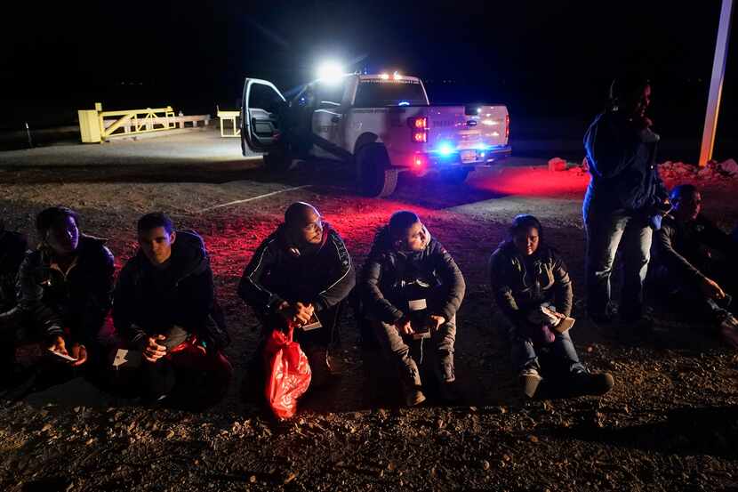 Varios migrantes esperan ser procesados por las autoridades estadounidenses luego de cruzar...