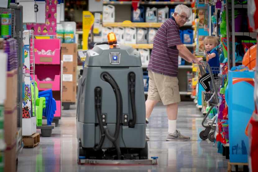 Customers watch the robotic floor scrubber clean an aisle at a North Richland Hills Walmart...